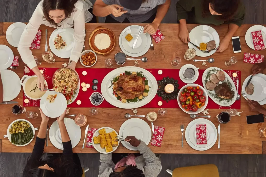 A group of people sitting at a table with turkey in the center and lots of food in a plate