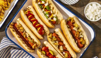 Turkey franks hot dogs placed topped with grilled vegetables placed in a tray.