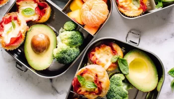 Three school lunch boxes with turkey pepperoni, avocado and fruits