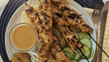Grilled turkey skewers with cucumbers, lemon and dip placed on a plate