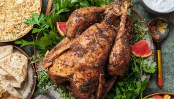 A middle eastern spiced whole turkey placed in the middle of the table with bread, rice and spices on the side.
